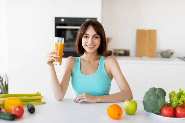 Zdrowa dieta. Szczęśliwa szczupła kobieta pije sok pomarańczowy, gotuje świeżą kolację, stoi w kuchni i uśmiecha się do kamery — Zdjęcie stockowe