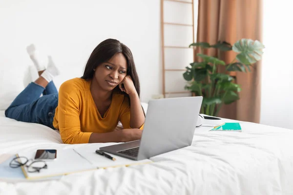 ベッドルームで寝そべっているノートパソコンを見る黒人女性 — ストック写真