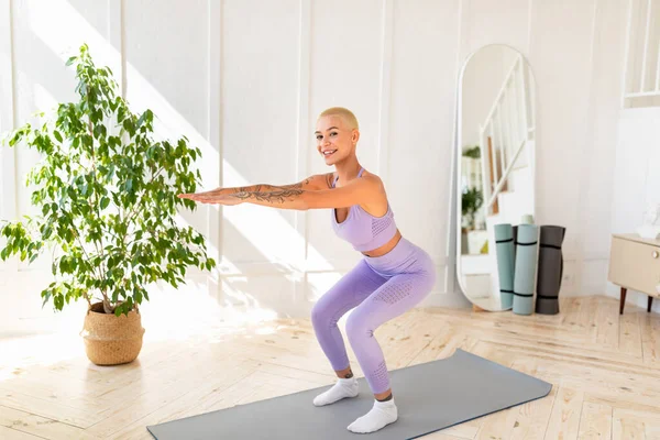 Portrait de jeune femme heureuse faisant des squats à la maison, effectuant des exercices de force, gardant en bonne forme — Photo