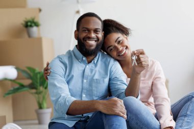 Neşeli, genç, Afro-Amerikan aile gösterisi anahtarı ve mukavva kutularla dolu bir odada gayrimenkul satın almanın keyfini çıkarın.