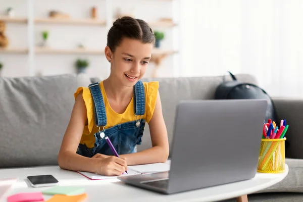 Веселий підліток сидить за столом, використовуючи ноутбук, малює в книзі — стокове фото
