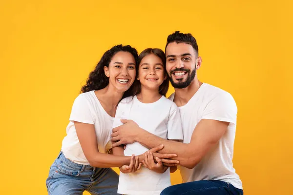 Pais felizes do Oriente Médio abraçando sua filha de criança em fundo amarelo — Fotografia de Stock