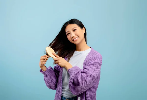 Cuidado del cabello y concepto de belleza. Feliz joven asiática señora cepillando su pelo sedoso oscuro natural con peine de madera —  Fotos de Stock