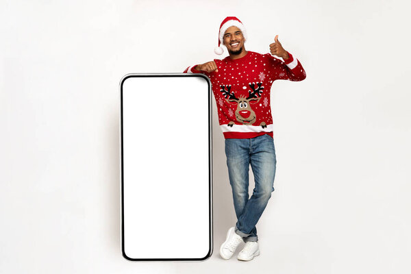 Smiling african american man in santa hat with big smartphone