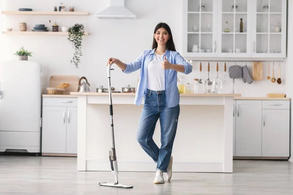 Szczęśliwa kobieta pokazuje kciuki w górę sprzątanie podłogi z mopem spray — Zdjęcie stockowe