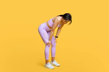 Spor, soluklan ve dinlen. Yorgun siyah kadın antrenmana ara veriyor, dizlerinin üzerine eğiliyor, sarı arka plan
