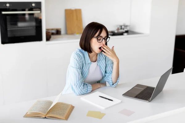Cansada dama soñolienta bostezar mientras trabaja o estudia en el ordenador portátil en línea desde casa, sentado en la cocina moderna, espacio libre —  Fotos de Stock