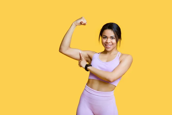 Concepto de resultados deportivos. Emocionada mujer afroamericana mostrando bíceps y señalándolo, fondo amarillo — Foto de Stock