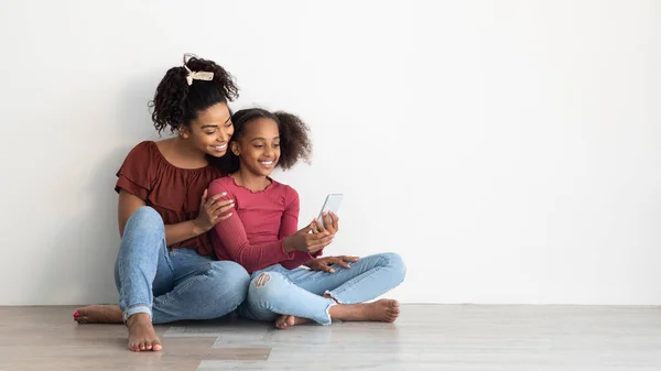 Mooie zwarte moeder en dochter met behulp van mobiele telefoon, panorama — Stockfoto