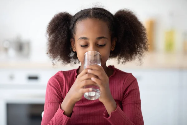 Svart jente drikker vann, kjøkkeninteriør – stockfoto