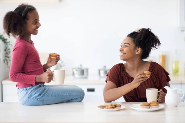 Alegre africana americana mamá e hija bebiendo té con cupcakes — Foto de Stock