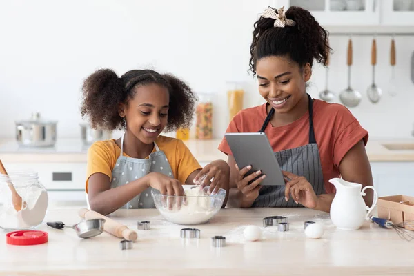 Happy black mother and daughter baking together, reading culinary blog