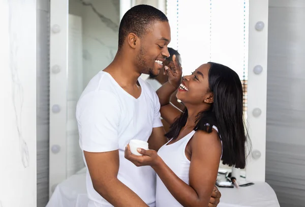 Cuidando negro esposa aplicación crema en maridos cara en cuarto de baño — Foto de Stock