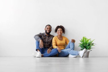 Afro-Amerikalı genç adam ve bayanın, beyaz duvarda saksıda otla yerde oturmasına sevindim.
