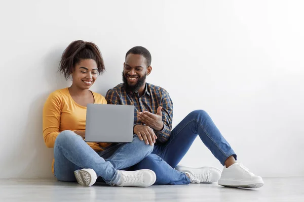 Ευτυχισμένη χιλιετή Αφροαμερικανός σύζυγος και σύζυγος χρησιμοποιούν το laptop για να σχεδιάσουν νέα εσωτερική διακόσμηση, κάθεται στο πάτωμα — Φωτογραφία Αρχείου