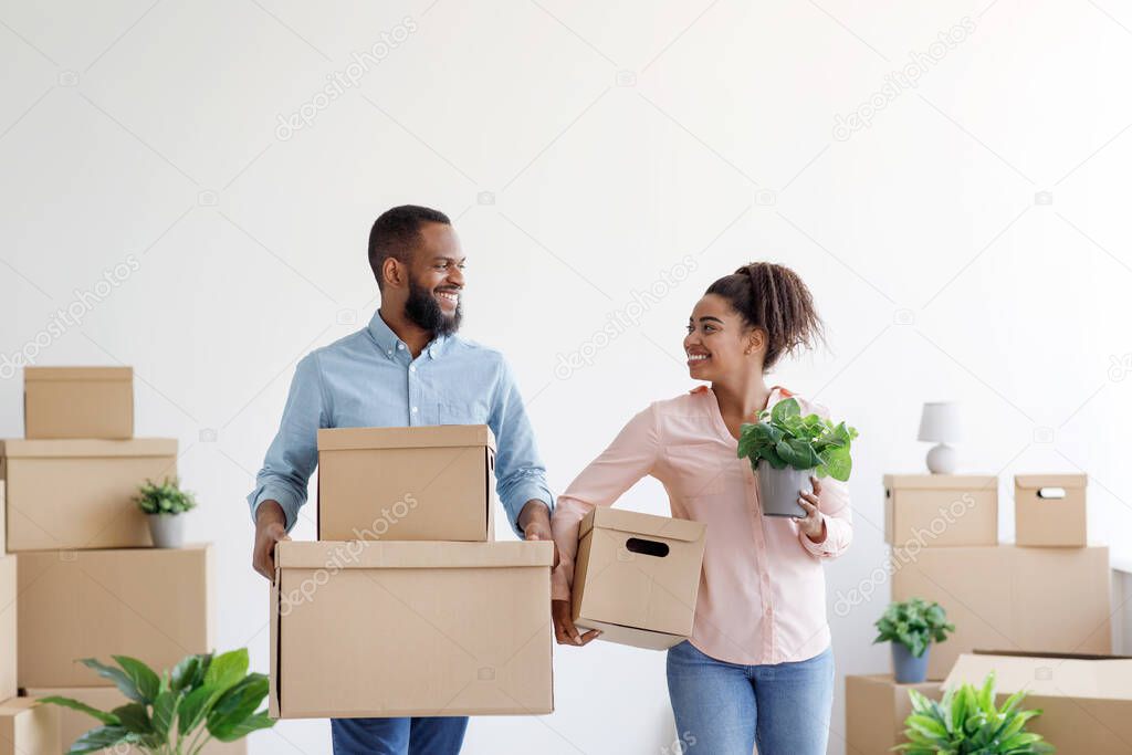 Happy young black man and woman carry cardboard boxes with things in room interior