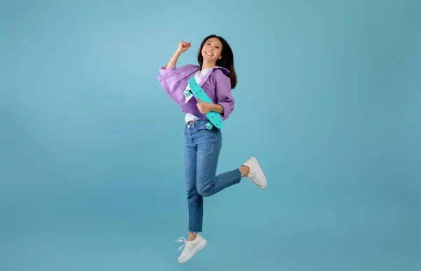 Teenage culture. Hravé asijské dáma s skateboard jumping a baví přes modré studio pozadí — Stock fotografie