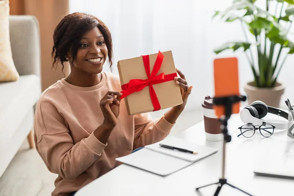 Černá žena ukazuje vánoční dárek k Smartphone tvorby videa uvnitř — Stock fotografie