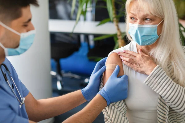 Seniorin wird gegen Covid geimpft, Krankenschwester trägt Klebeverband auf — Stockfoto