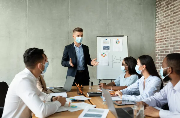 Reunión de negocios pandémica. Empresario en máscara teniendo conferencia con compañeros de trabajo en oficina — Foto de Stock