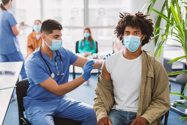 Blck Guy recevant l'injection de vaccin contre le coronavirus assis avec le médecin à l'intérieur — Photo