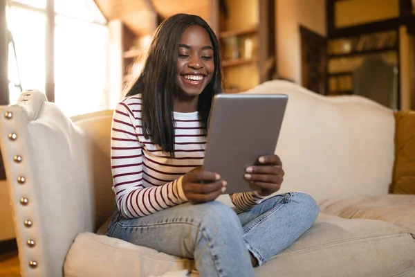 Lächelnde junge schwarze Frau mit digitalem Tablet, zu Hause auf Couch sitzend, leerer Raum — Stockfoto