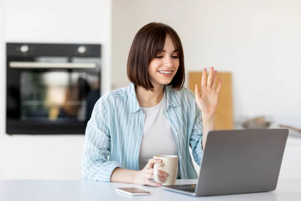 Comunicação online. Jovem freelancer do sexo feminino conversando na webcâmera laptop e beber café, sentado na cozinha — Fotografia de Stock