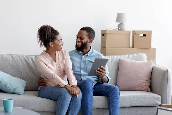 Glad ung svart man och kvinna koppla av på soffan med hjälp av surfplatta för online köpa möbler — Stockfoto