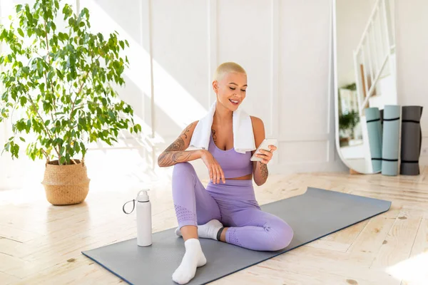 Aktives Lebensstilkonzept. Junge Frau entspannt sich nach dem Heimtraining auf Yogamatte mit Smartphone — Stockfoto