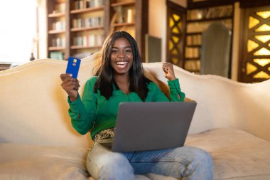 Büyük kumarhane kazancı, büyük online satış. Kredi kartı ve dizüstü bilgisayarı olan genç siyahi kadın indirimli alışveriş yapıyor, piyango kazanıyor.