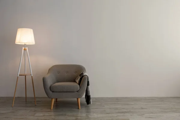 Semplice poltrona con plaid, lampada incandescente sul pavimento su sfondo grigio parete in soggiorno — Foto Stock
