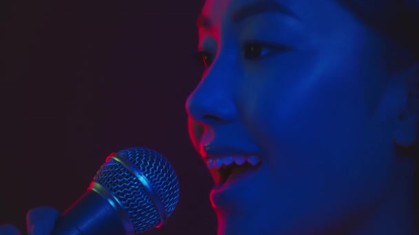 Профессиональный. Портрет молодой вдохновлённой азиатки, поющей красивую песню в микрофон в фиолетовых неоновых огнях — стоковое видео