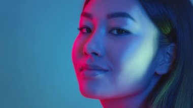 Moda güzeli. Genç pozitif Asyalı kadın yüzünü kameraya çeviriyor ve gülümsüyor. Parlak neon ışıklar, boş alan.