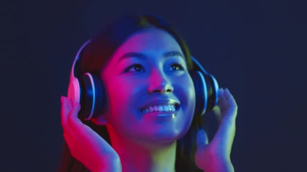 Любимая музыка онлайн. Портрет счастливой азиатки, наслаждающейся прекрасной музыкой в современных беспроводных наушниках и танцами — стоковое видео