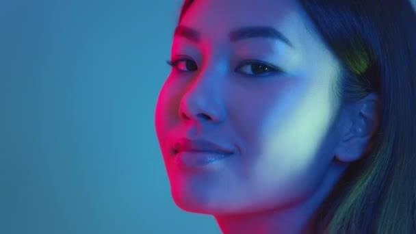 Beleza da moda. Jovem mulher asiática positiva virando o rosto para a câmera e sorrindo, luzes de néon brilhantes, espaço vazio — Vídeo de Stock