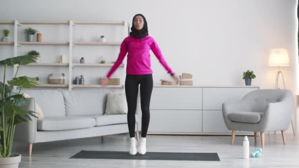 Cardio training at home. Young cheerful arab woman wearing traditional hijab practicing jumping jack exercise — Stock Video