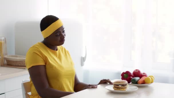 Valsspelen. Opgewonden overgewicht zwarte vrouw kiezen om cheeseburger eten over groenten — Stockvideo