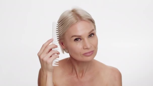 Vacker medelålders kvinna borsta hår med kam och titta på kameran — Stockvideo