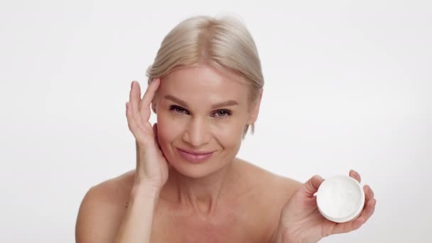 Концепція догляду за шкірою. Красива усміхнена жінка середнього віку тримає Джар з зволожуючим кремом — стокове відео