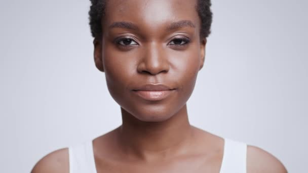 Retrato de belleza de una joven modelo afroamericana mirando a la cámara, fondo gris del estudio, cámara lenta — Vídeo de stock