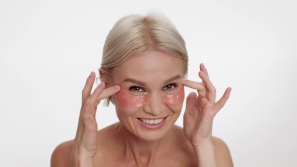 Corvos Pés Tratamento. Mulher de meia-idade bonita aplicando adesivos de colágeno sob os olhos — Vídeo de Stock