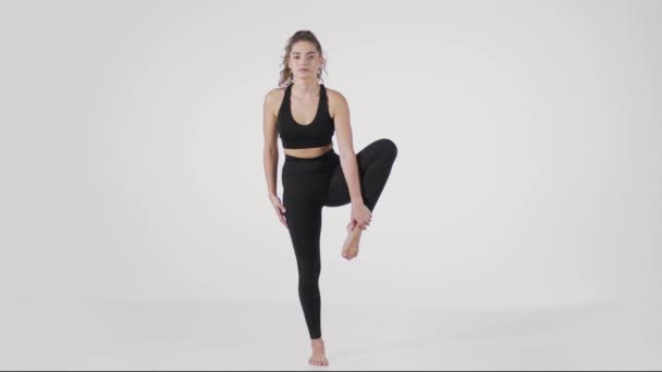 Μαθήματα γιόγκα. Νεαρή αθλητική γυναίκα στέκεται στο ένα πόδι και gesturing namaste, αποδεικνύοντας τη βασική στάση asana — Αρχείο Βίντεο