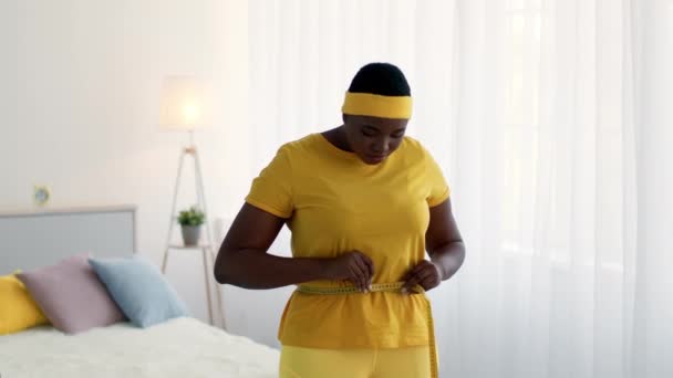Overvægtige sorte kvinde måling talje med tape derhjemme, ked af det med resultatet – Stock-video
