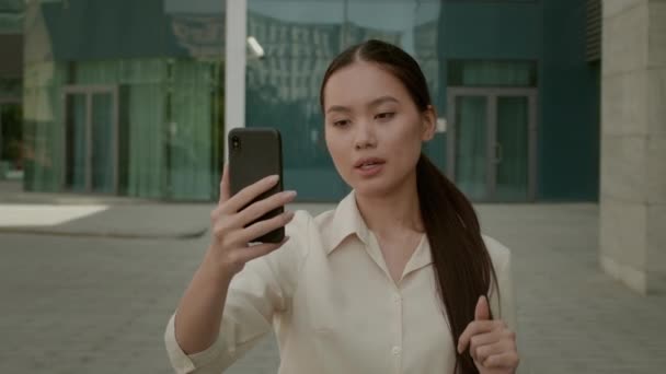 Mujer de negocios asiática haciendo videollamada a través de Smartphone caminando fuera — Vídeos de Stock