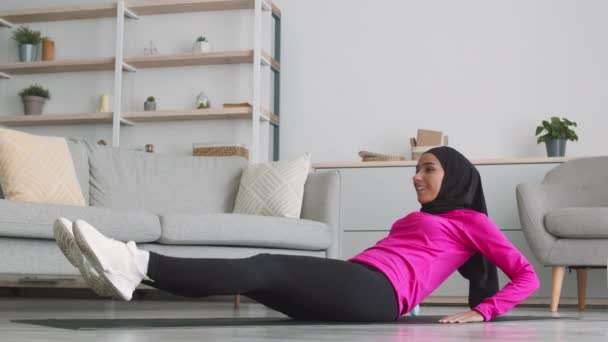 Jovem mulher positiva do Oriente Médio no hijab praticando exercícios musculares abdominais, deitada no chão e fazendo crunches — Vídeo de Stock