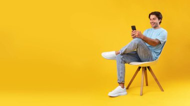 Stüdyoda cep telefonu kullanan mutlu adam, sandalyede oturuyor, afiş yapıyor.