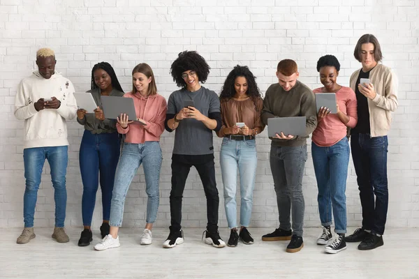 International group of young men and women using different gadgets