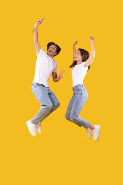 Eccitato coppia millenaria prendere selfie e saltare in studio — Foto Stock
