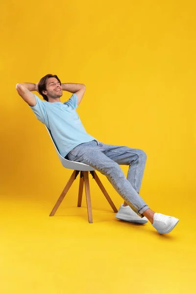 Mutlu adam sandalyeye oturmuş, stüdyoda arkasını yaslıyor. — Stok fotoğraf