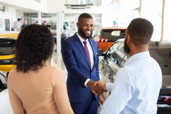 Autókereskedés koncepció. Eladó Kézfogás fiatal fekete vásárlókkal pár a bemutatóteremben — Stock Fotó